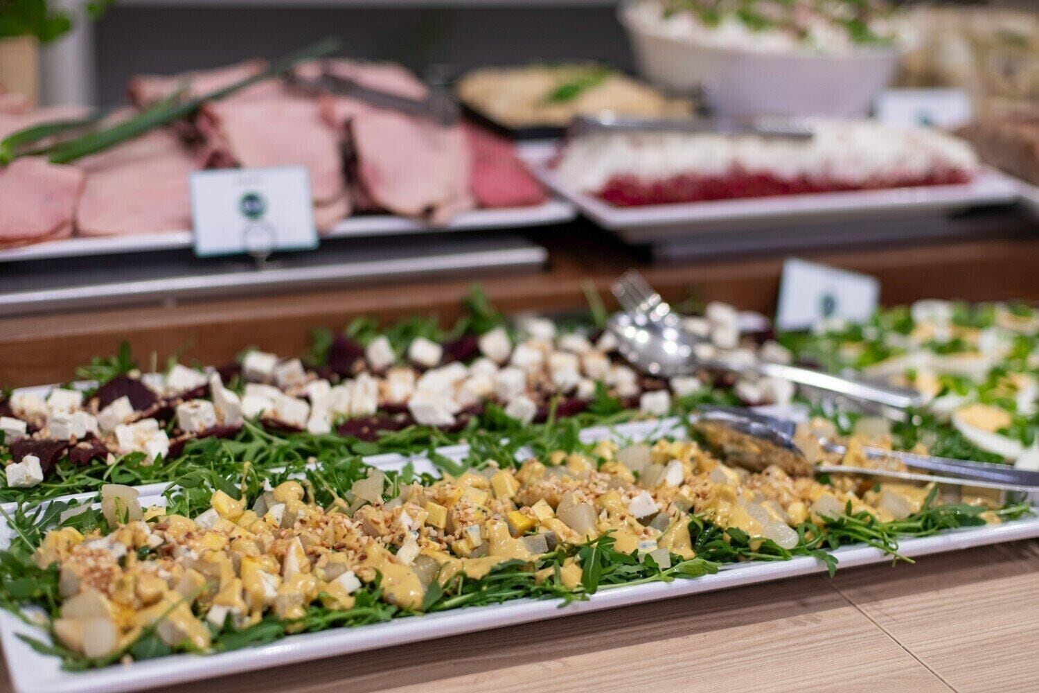 A buffet with various dishes including salads, meats, and cheeses.
