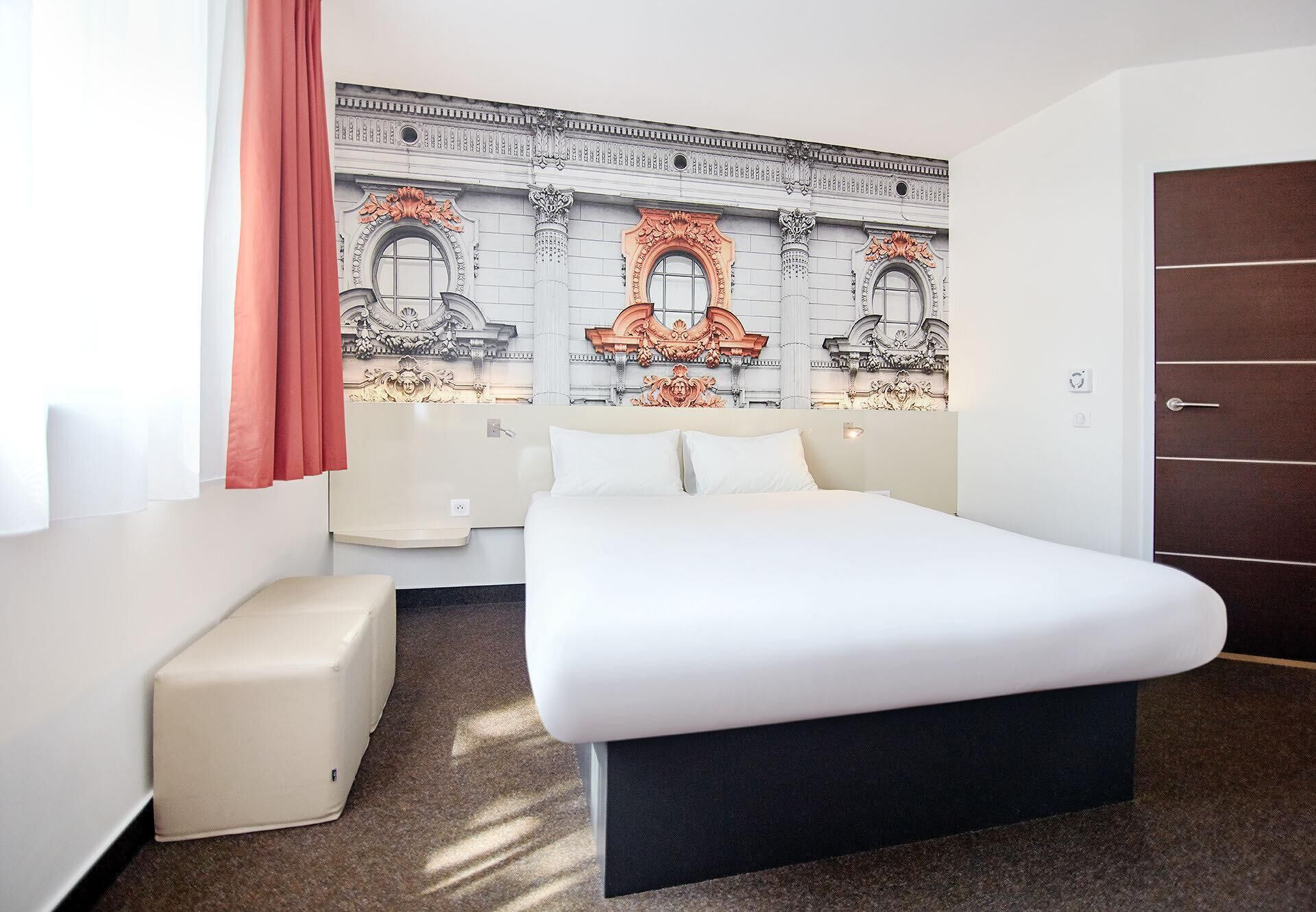 A hotel room with a large bed, a small sofa, a decorative wall mural, and a door.