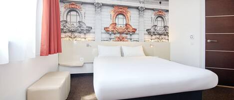 A hotel room with a large bed, a small sofa, a decorative wall mural, and a door.