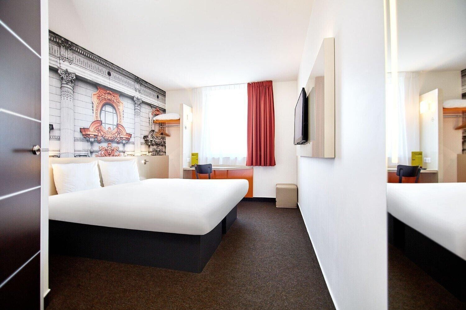 Une chambre d’hôtel avec un grand lit, un bureau, une chaise, une télévision et une fenêtre avec des rideaux.