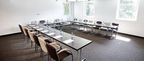 Un salón de conferencias con una larga mesa, sillas y un proyector.