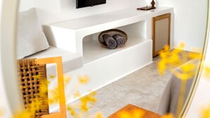 A modern living room with a flat-screen TV mounted on a white console, a small plant, and a woven basket on the console. - Anemomylos Residence (Paros)