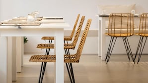 A modern dining area with a white table, wicker chairs, and pendant lighting. - Anemomylos Residence (Paros)