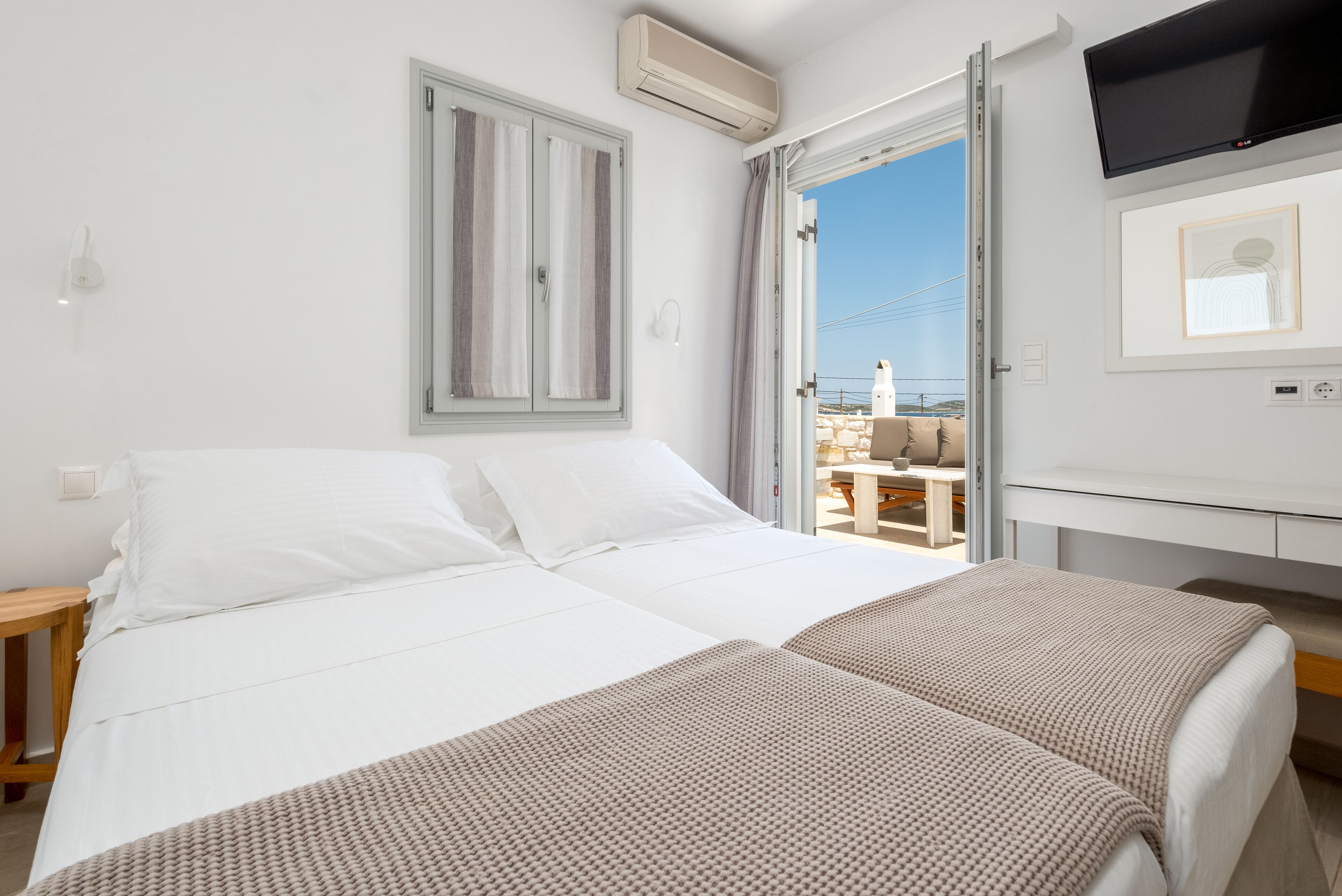 A hotel room with a bed, a TV, and a view of the sea.