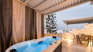 An outdoor hot tub area with a pergola, stone wall, and a dining table with chairs. - Anemomylos Residence (Paros)