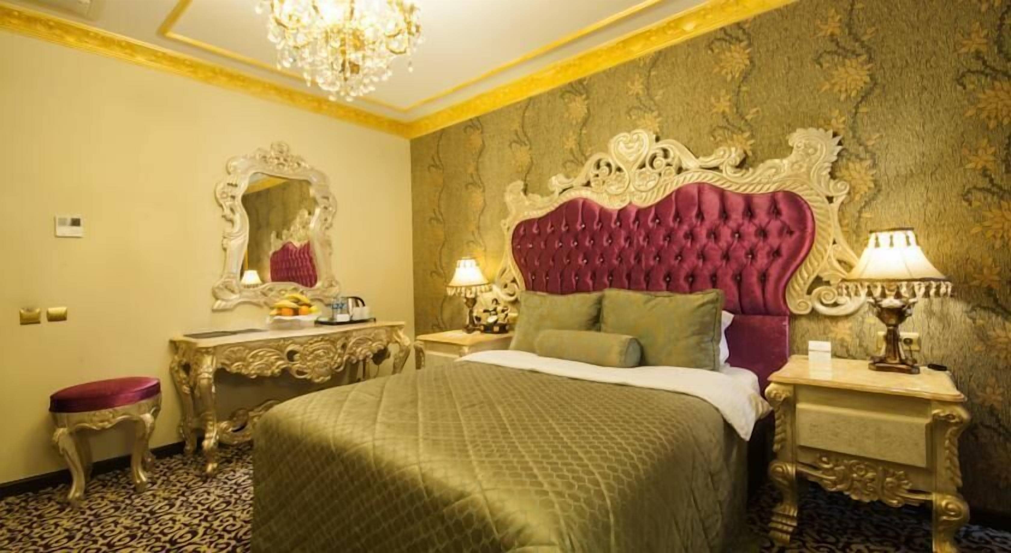 Una lujosa habitación de hotel con una cama grande, un cabecero decorado, un espejo y dos mesitas de noche con lámparas.