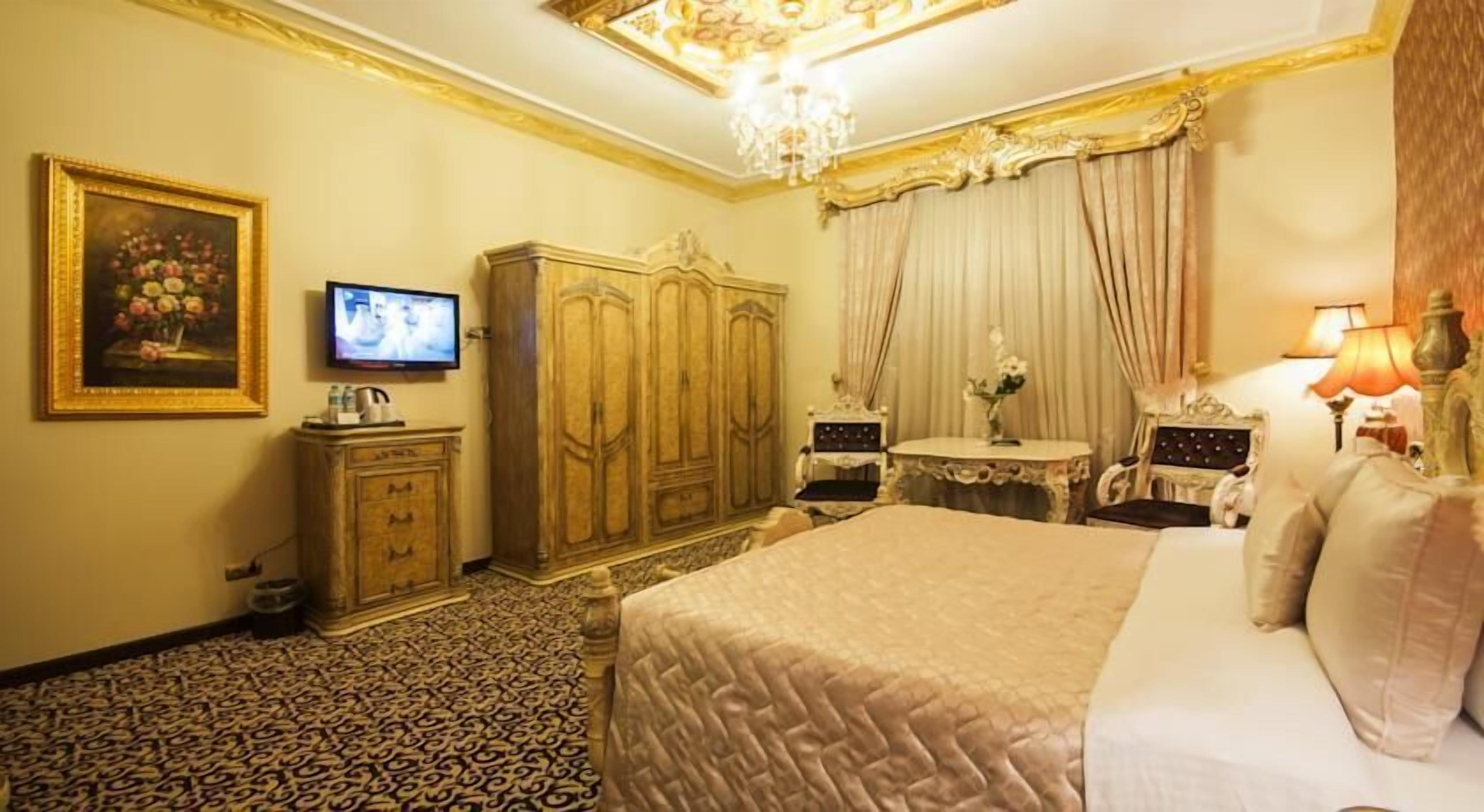 A hotel room with a large bed, a television, a wardrobe, a small table with a lamp, and a painting on the wall.