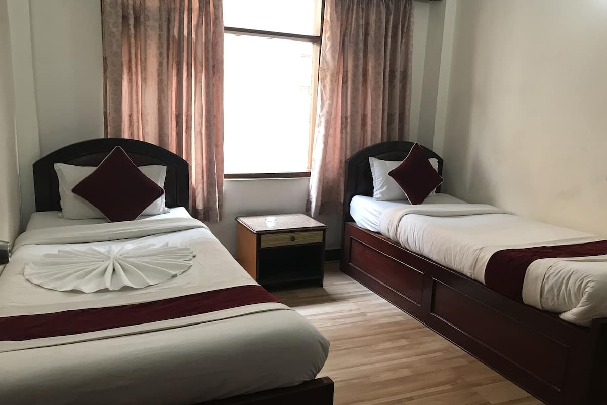 A hotel room with two single beds, a nightstand, and a window with curtains.