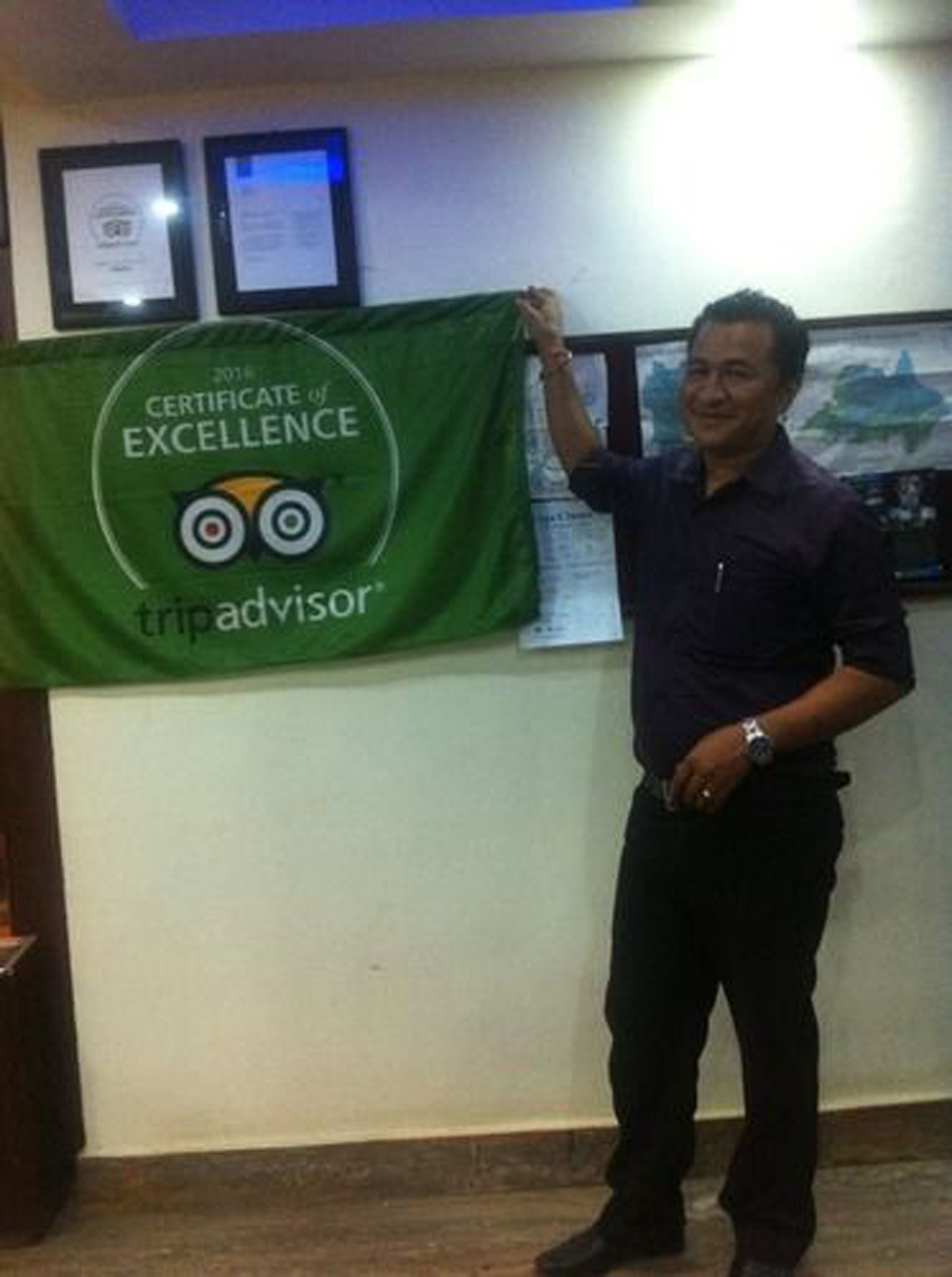 A person holding a certificate of excellence banner with the TripAdvisor logo.