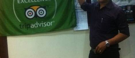 A person holding a certificate of excellence banner with the TripAdvisor logo.
