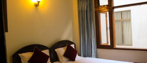 A hotel room with a bed, a wall-mounted light, a window with curtains, and a towel on the bed.