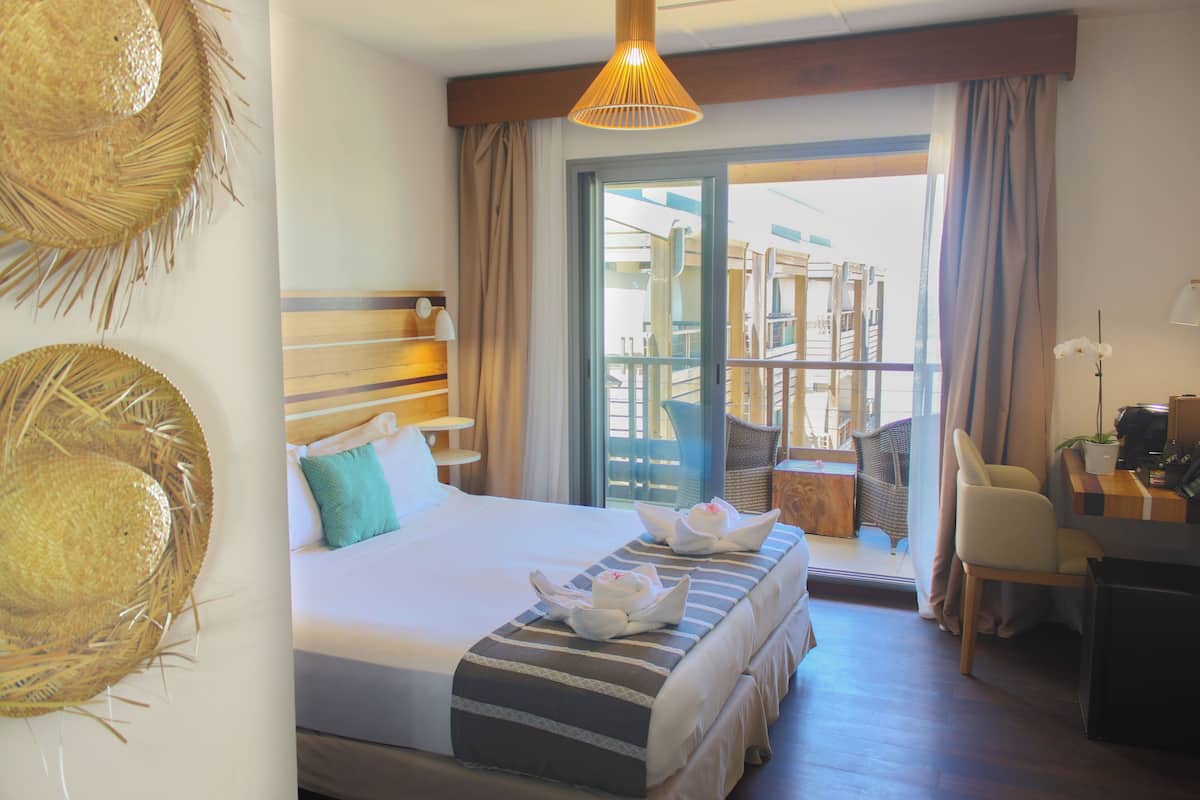 Une chambre d’hôtel comprenant un lit, un bureau, une chaise, un balcon avec vue et un luminaire suspendu.
