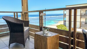 A balcony with a wicker chair, a small wooden table with a cup and a plant, and a view of the ocean. - Le Battant Des Lames (Saint-Pierre)