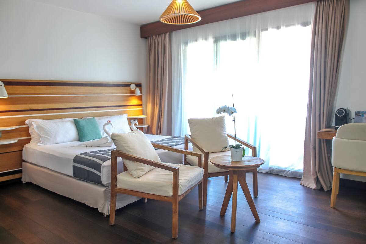 Une chambre d’hôtel avec un lit, deux fauteuils, une petite table et une lampe.