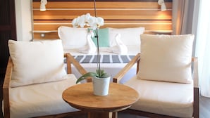 A hotel room with a bed, two white chairs, a round wooden table with a potted orchid, and a wooden headboard with two wall-mounted lights. - Le Battant Des Lames (Saint-Pierre)