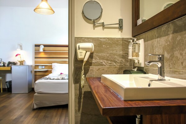 Una habitación de hotel con cama, un escritorio pequeño, secador de pelo, espejo y lavamanos.