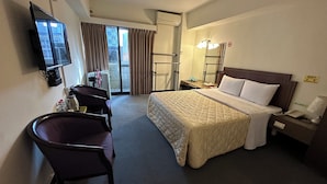 Een hotelkamer met een bed, bureau, stoel, televisie en een raam met gordijnen.
