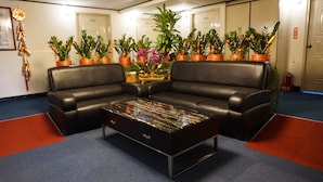 Een hal met een zwarte leren bank, een glazen salontafel en potplanten.
