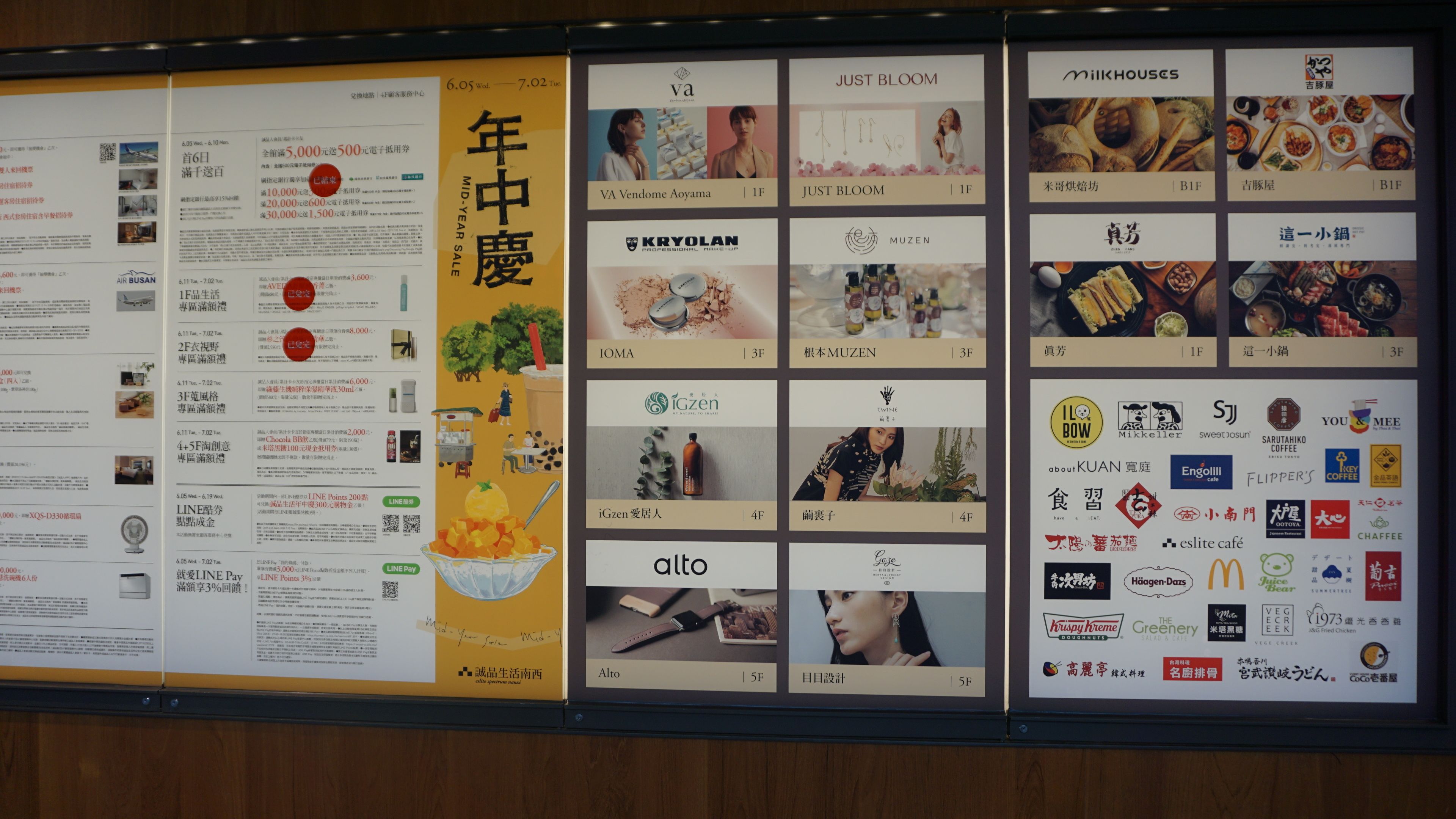 A promotional display board with various advertisements and logos, including a mid-year sale, professional makeup, and food brands.