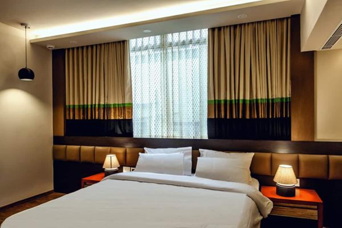 A hotel room with a large bed, two bedside tables with lamps, a headboard, and a window with curtains.