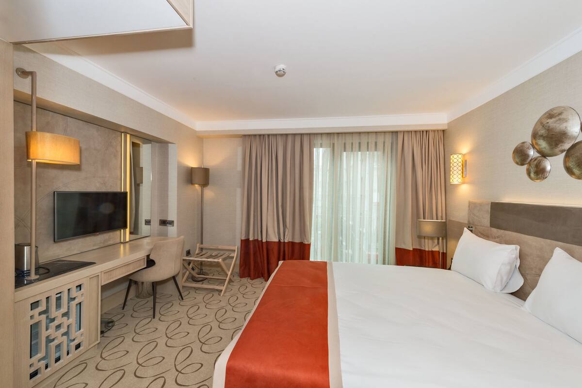 A hotel room with a bed, a desk, a chair, a TV, and a window with curtains.