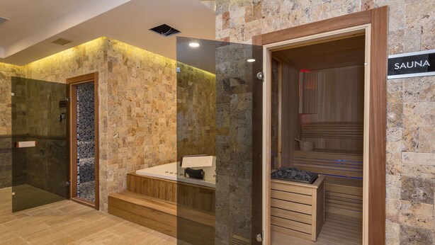 Un moderno espacio de spa con pared de piedra, sauna de madera y ducha con cerramiento de vidrio.