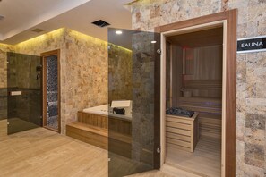 Un moderno espacio de spa con pared de piedra, sauna de madera y ducha con cerramiento de vidrio.