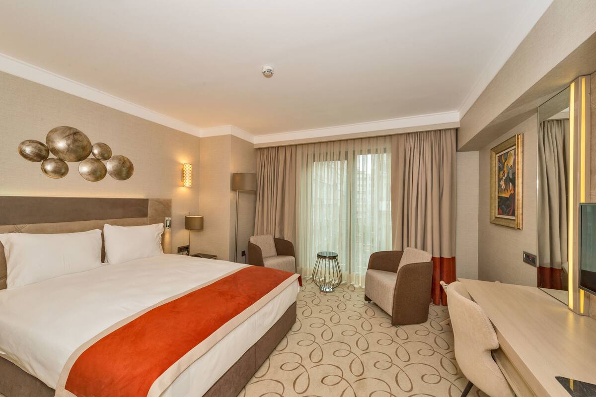 A hotel room with a large bed, two armchairs, a small table, and a TV.