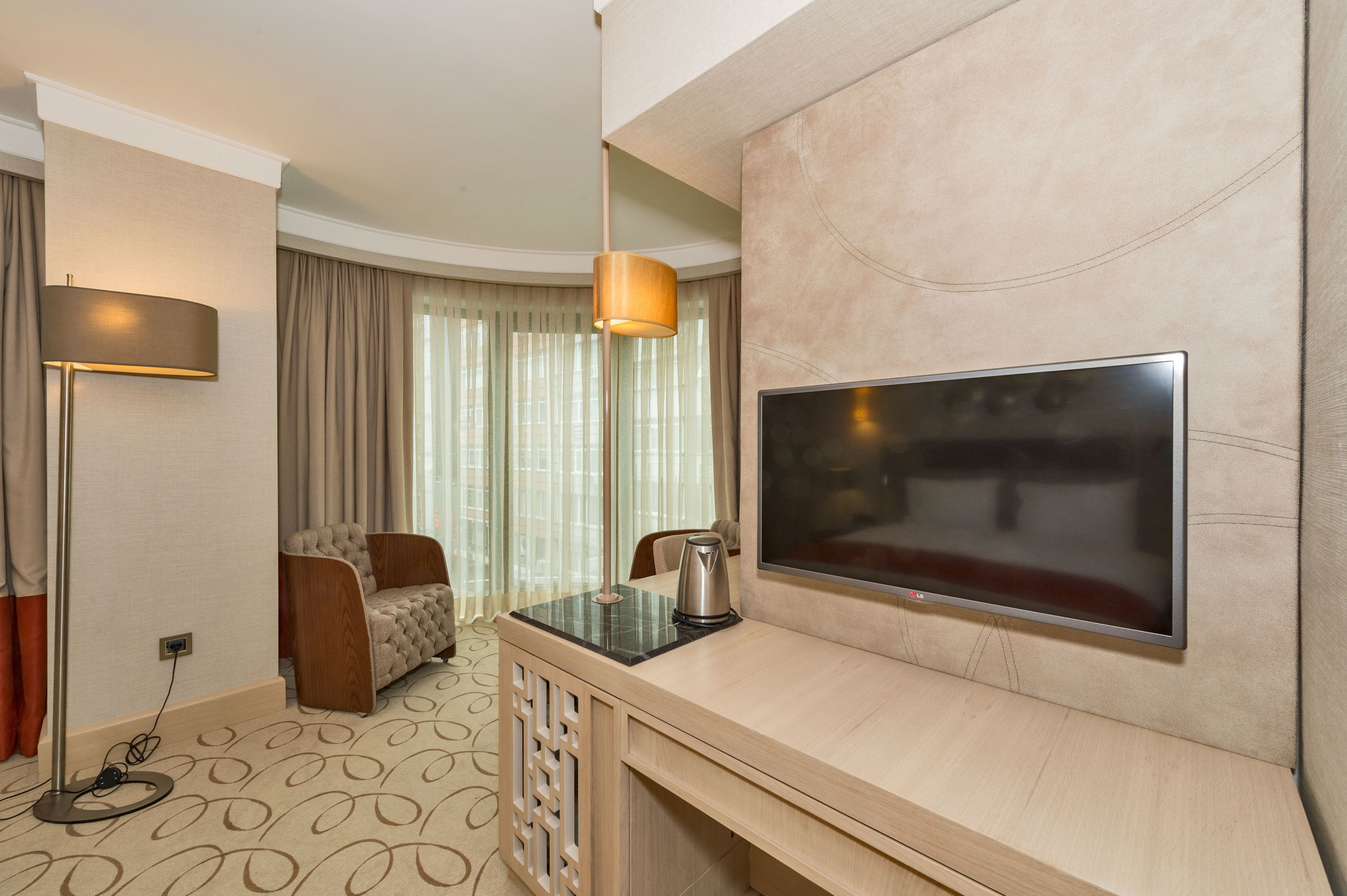 A hotel room with a flat-screen TV mounted on the wall, a sofa, a coffee table, and a lamp.
