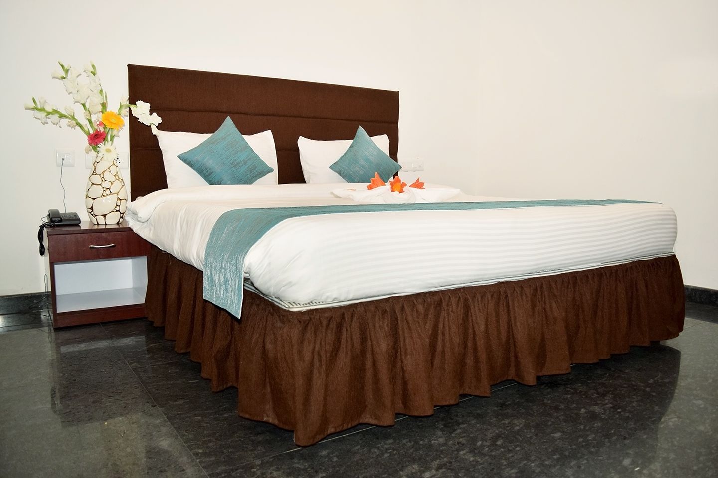 A neatly made bed with a brown headboard, white bedding, and teal accent pillows.