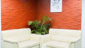 A corner room with a red brick wall, two white sofas, a glass coffee table, and a framed picture on the wall.
