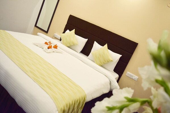A neatly made bed with white linens and a yellow striped blanket, a dark headboard, and white pillows. - The Verda Prakyathi (Bengaluru)