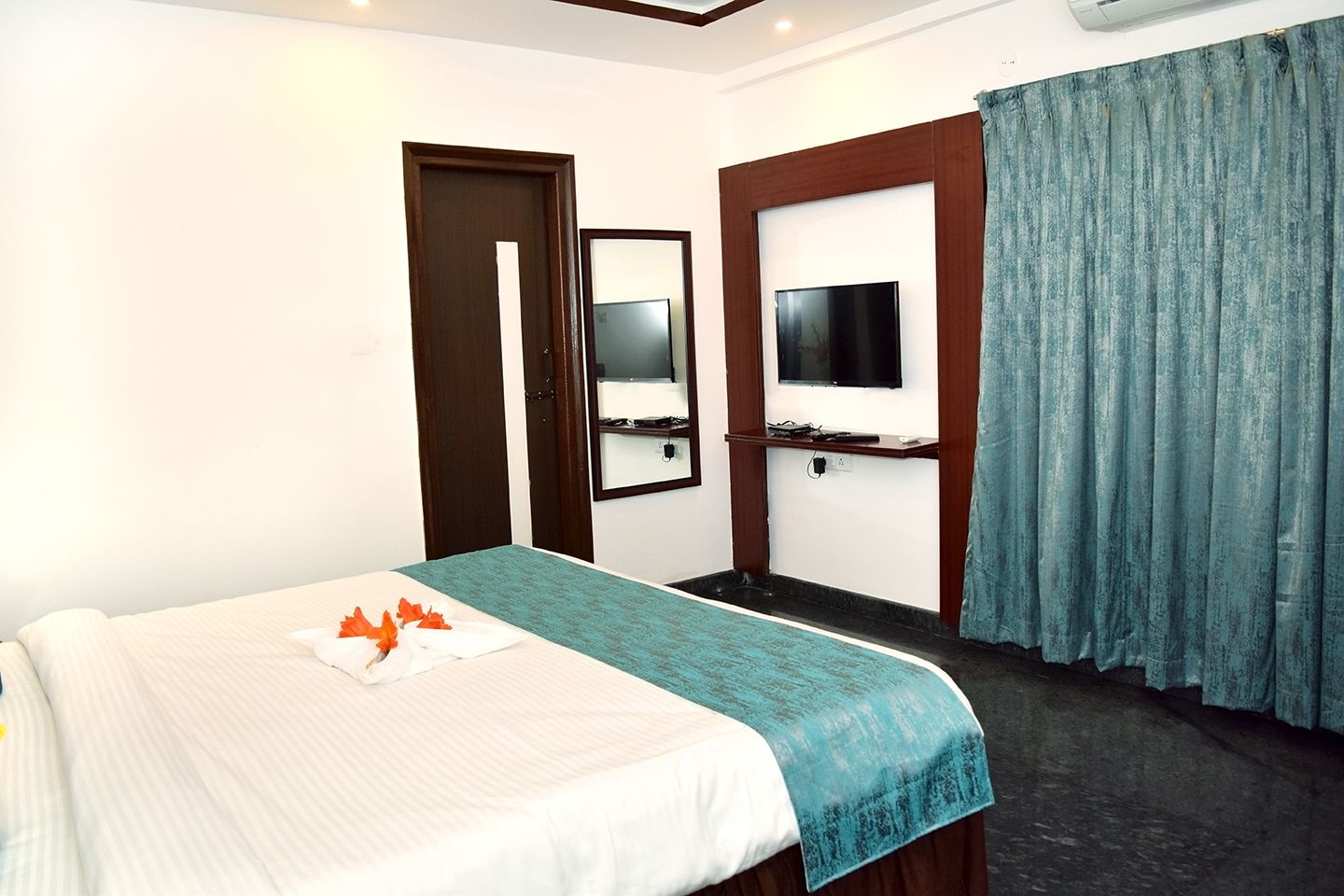 Une chambre d’hôtel avec un lit, une télévision, un miroir et une fenêtre avec des rideaux.