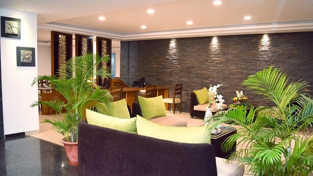 Eine moderne Lobby mit einer dunklen Steinwand, einer Sitzecke mit Sofa und Sesseln sowie Zimmerpflanzen.
