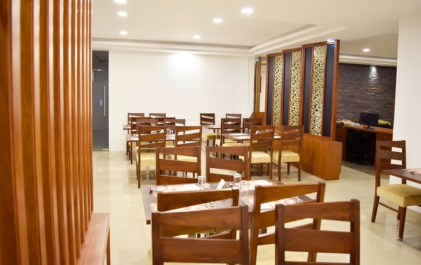 Un espace repas avec des tables et des chaises en bois, un paravent décoratif et un bureau avec un ordinateur.