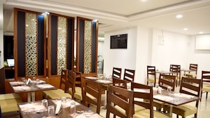 Ein Restaurant mit Holztischen und -stühlen, einem dekorativen Raumteiler und einem gerahmten Kunstwerk an der Wand.