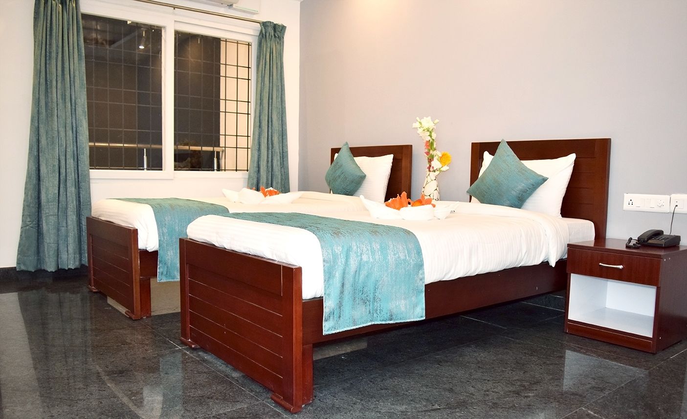Habitación de hotel con dos camas de madera, una mesita de noche y un ventanal con cortinas.