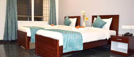 Habitación de hotel con dos camas de madera, una mesita de noche y un ventanal con cortinas.