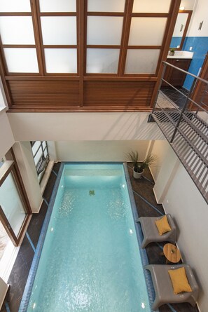 Piscina con techo de madera y una pequeña zona de estar con cojines.