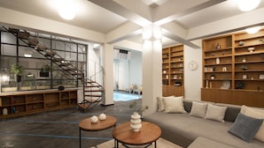 A modern living room with a staircase, a pool, and a large bookshelf. - Villa Meliti (Athens)