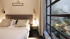 A bedroom with a bed, bedside lamps, a window with a view of plants outside. - Villa Meliti (Athens)