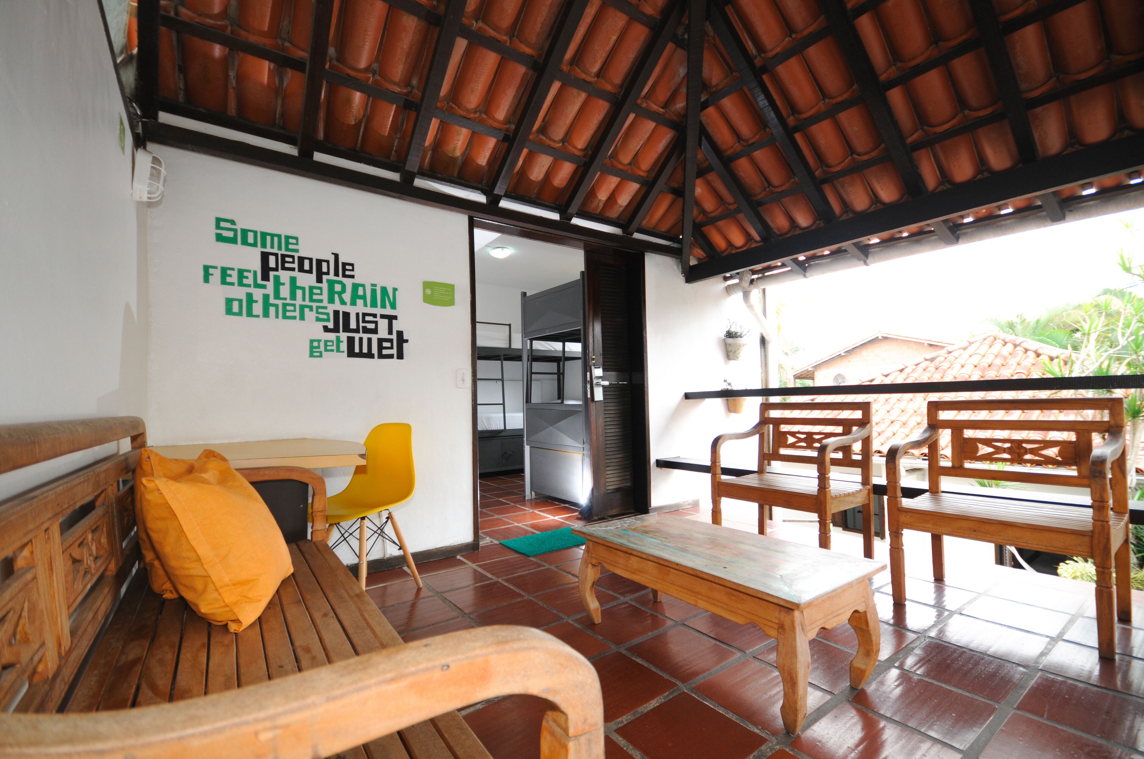 A wooden bench with a yellow cushion, a wooden table, and a wooden chair. There is a wall with a motivational quote.