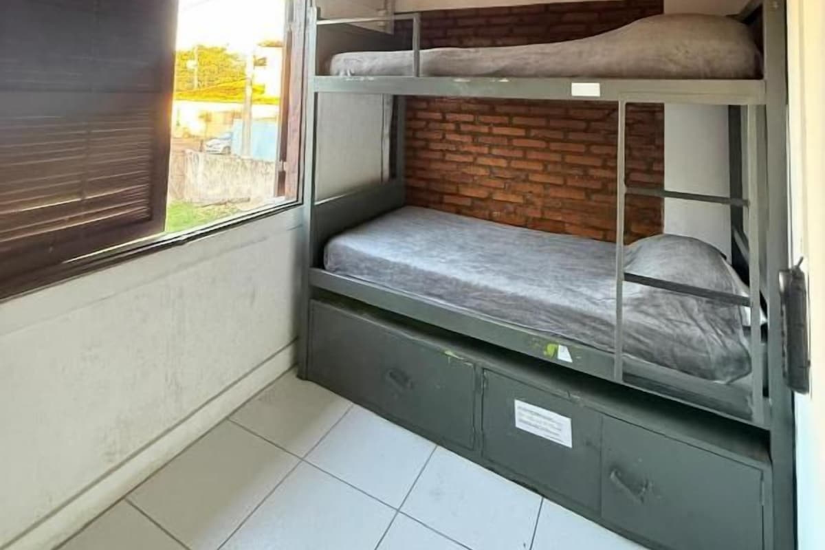 Habitación con literas, techo de madera, ventana y pared de ladrillo.
