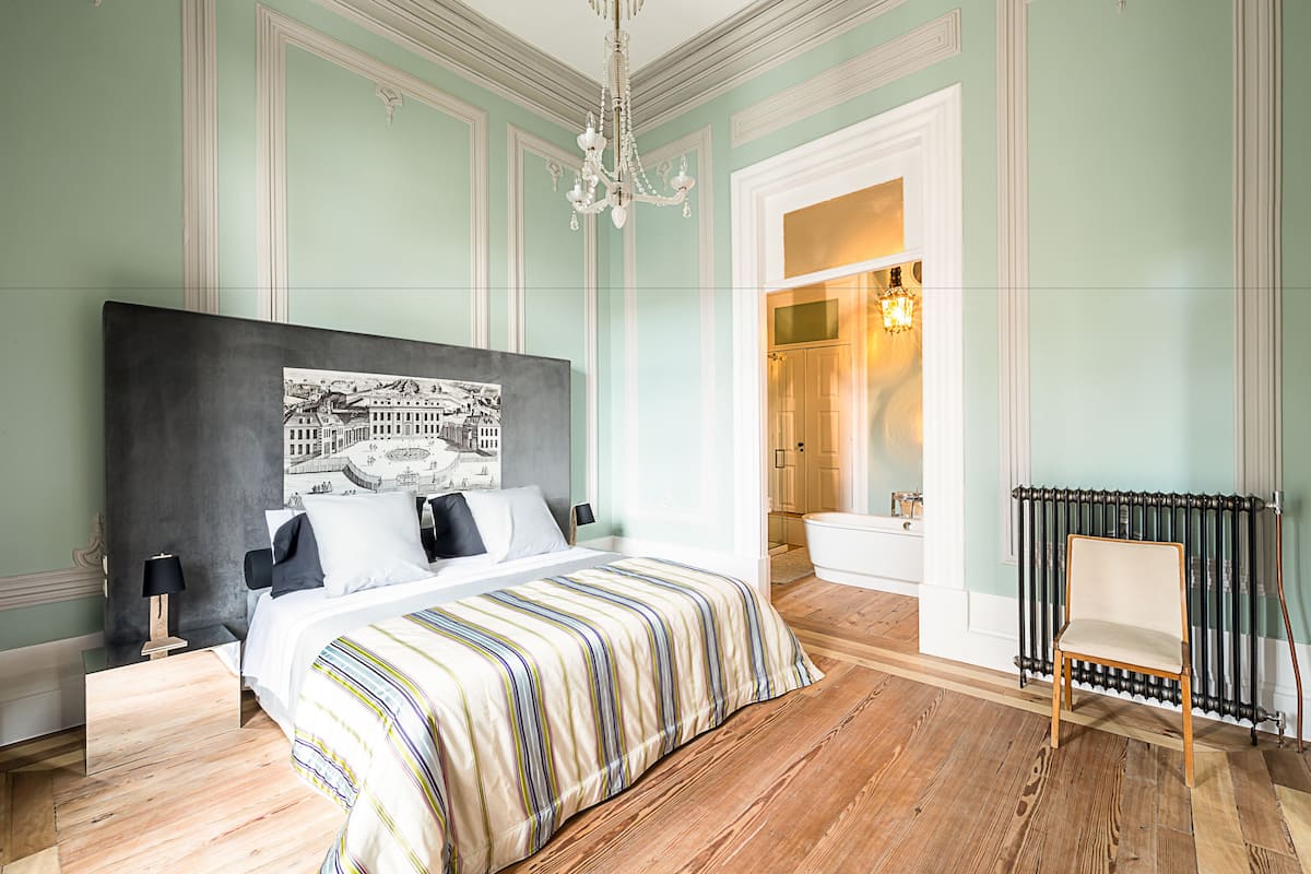 A bedroom with a large bed, a wooden floor, a radiator, and a chair.