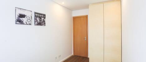 A room with a bed, a green rug, a wooden door, and two posters on the wall.