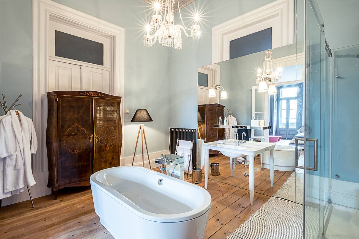 A spacious bathroom with a freestanding bathtub, a large mirror, and a chandelier.