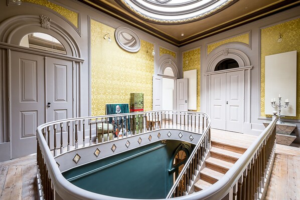 Una imponente escalera con mesa de billar, puertas blancas decoradas y un candelabro.
