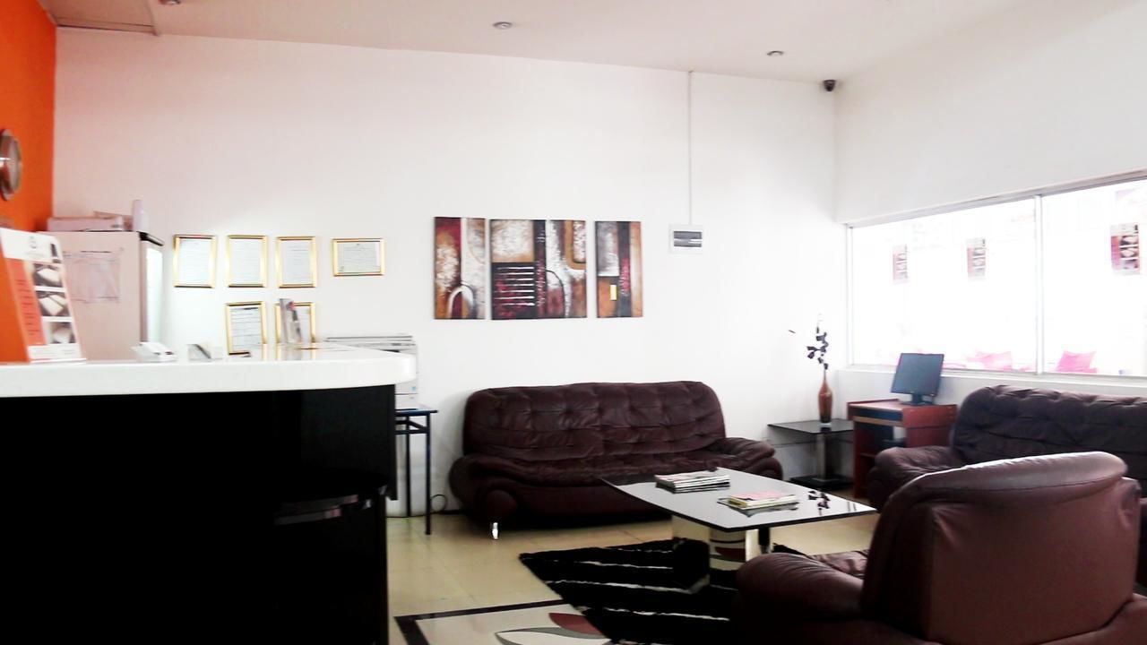 A modern living room with a dark brown sofa, a coffee table, and a TV. There are framed pictures on the wall and a window with a view of the city.