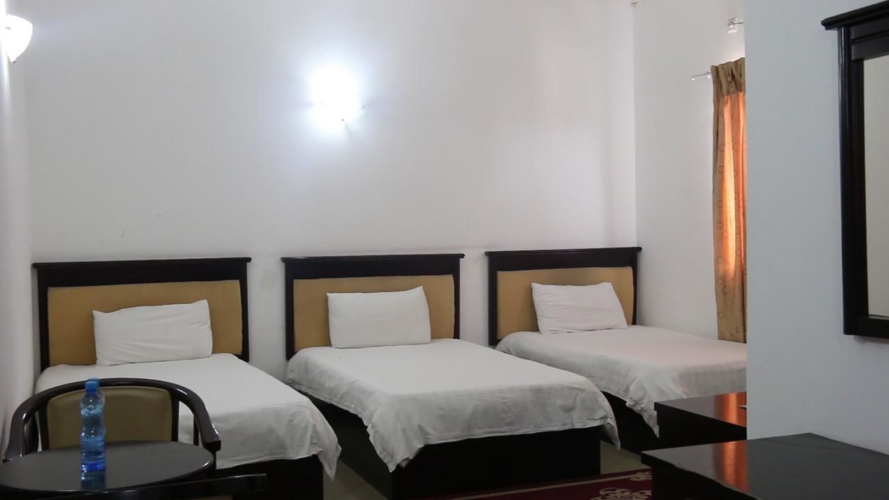 Habitación de hotel con tres camas individuales, una mesita con una silla y una botella de agua sobre la mesita.