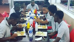 A group of people seated at a table with food and condiments, in a room with red chairs and a window. - Hotel Al-Khalil Machava (Matola)